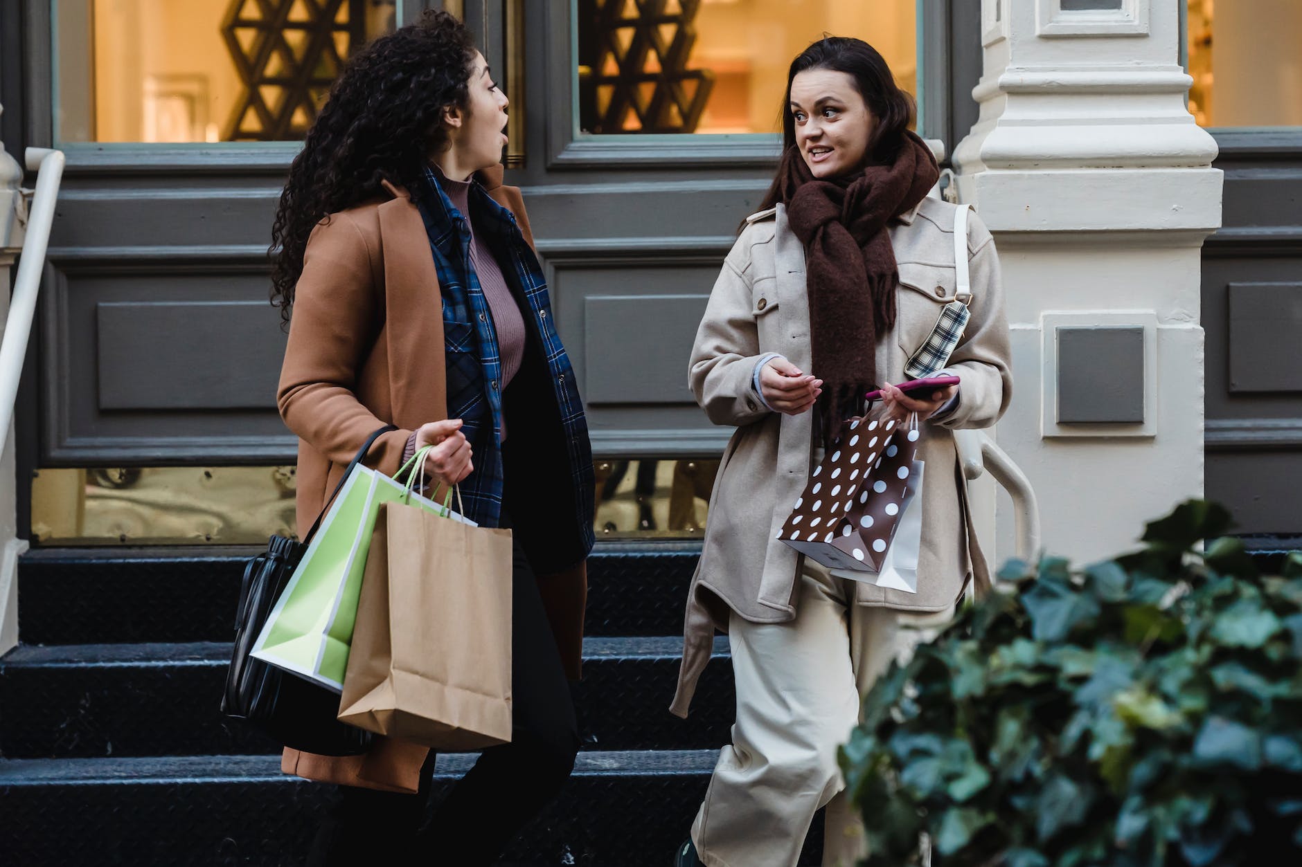 amazed young multiracial women gossiping while strolling on street with shopping bags