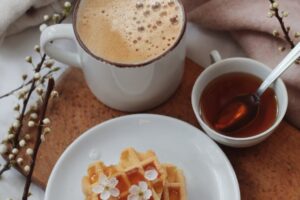 cup of cacao with waffles and honey served on bed near gentle flowers